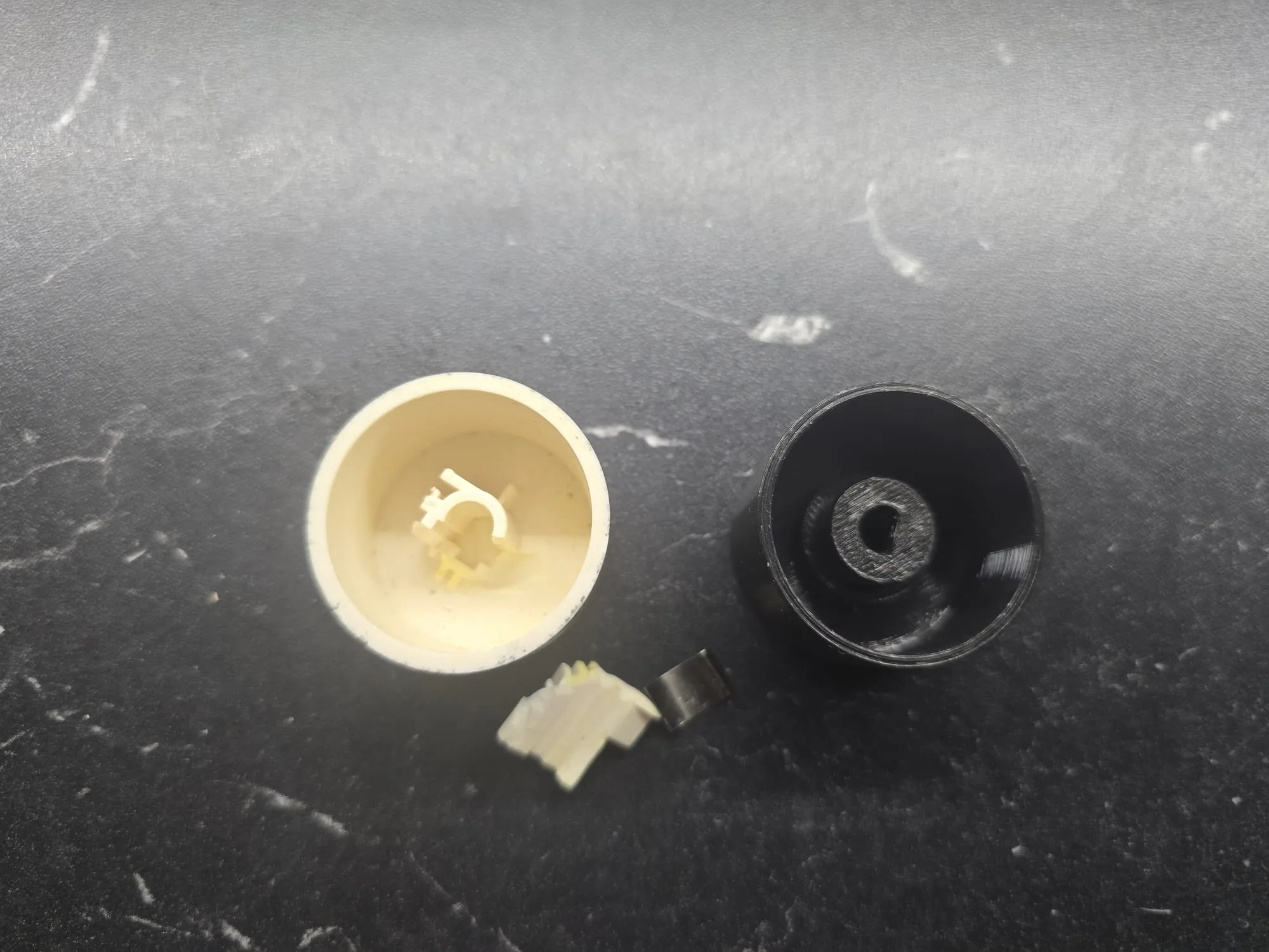Puknuti bijeli tvornički kotačić nape i novi crni kotačić izrađen 3D printom od PETG-a